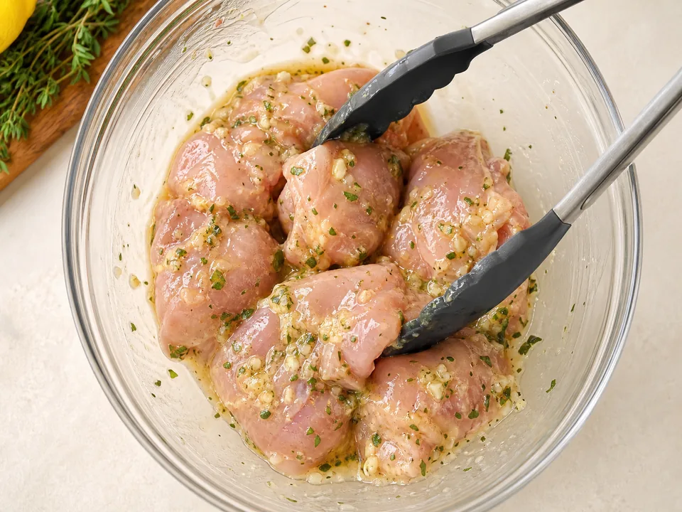 Raw boneless chicken thighs safely contained in a bowl and coated with lemon herb oil